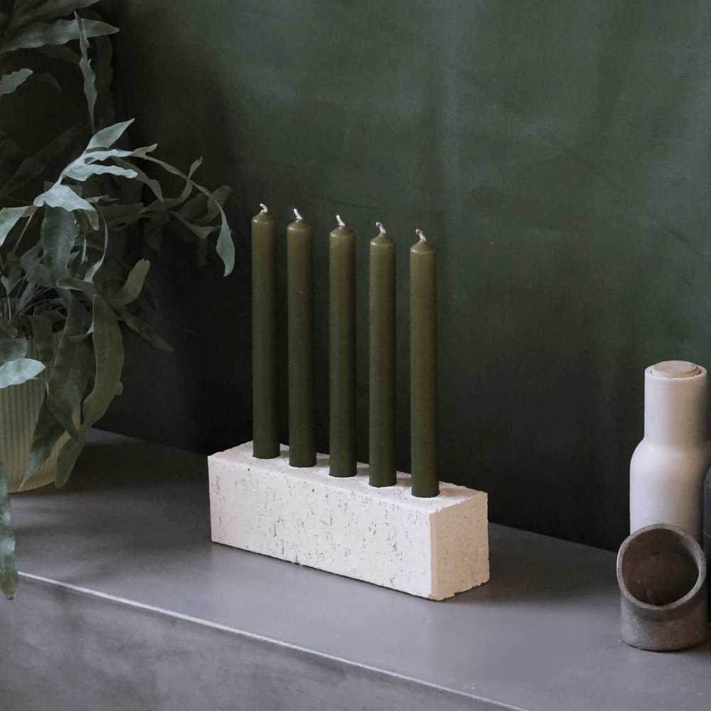 White centrepiece candleholder on a green backdrop. The candleholder is made from a recycled sand brick. It houses 5 candles in the olive colour way.