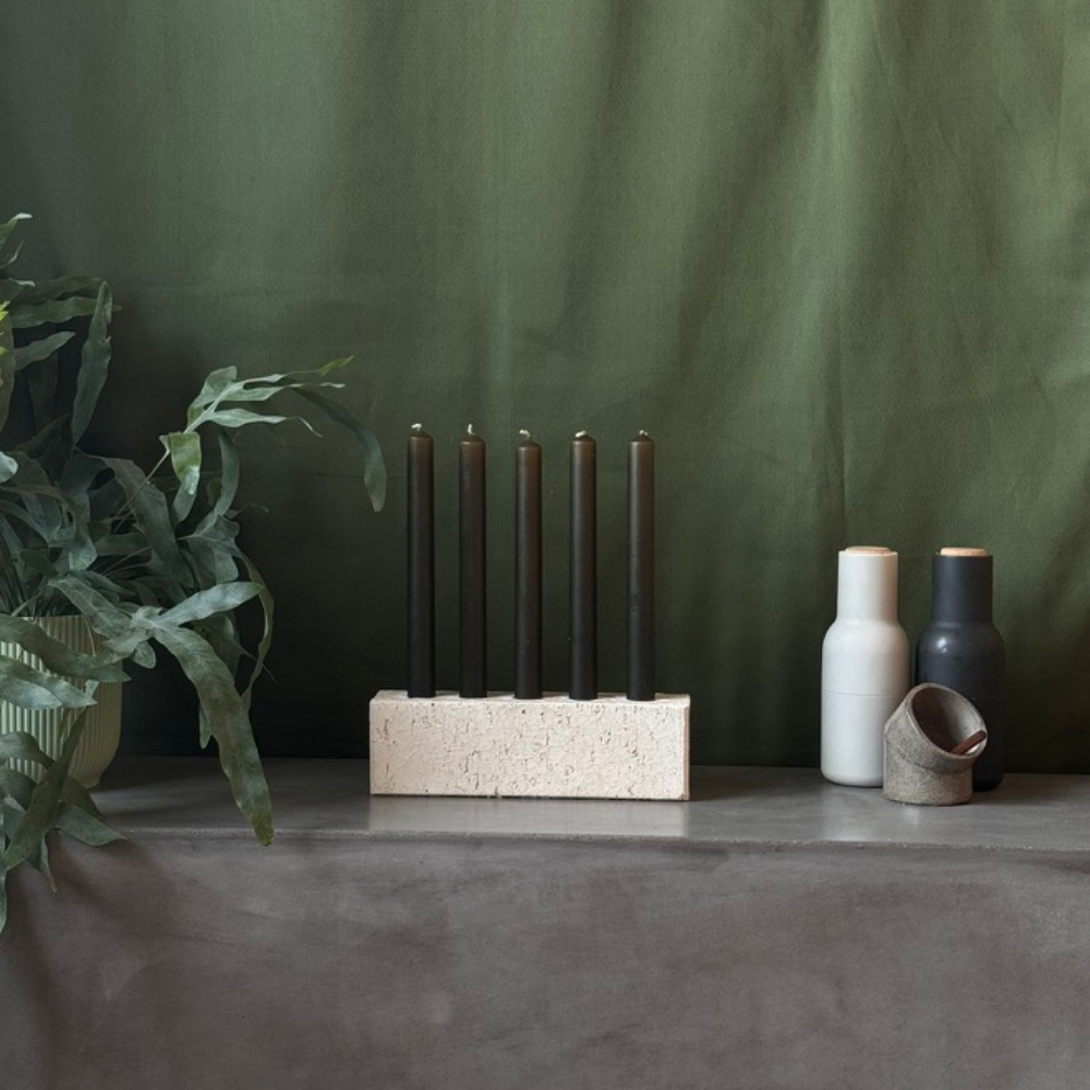 White centrepiece candleholder on a green backdrop. The candleholder is made from a recycled sand brick. It houses 5 candles in the licorice colour way.